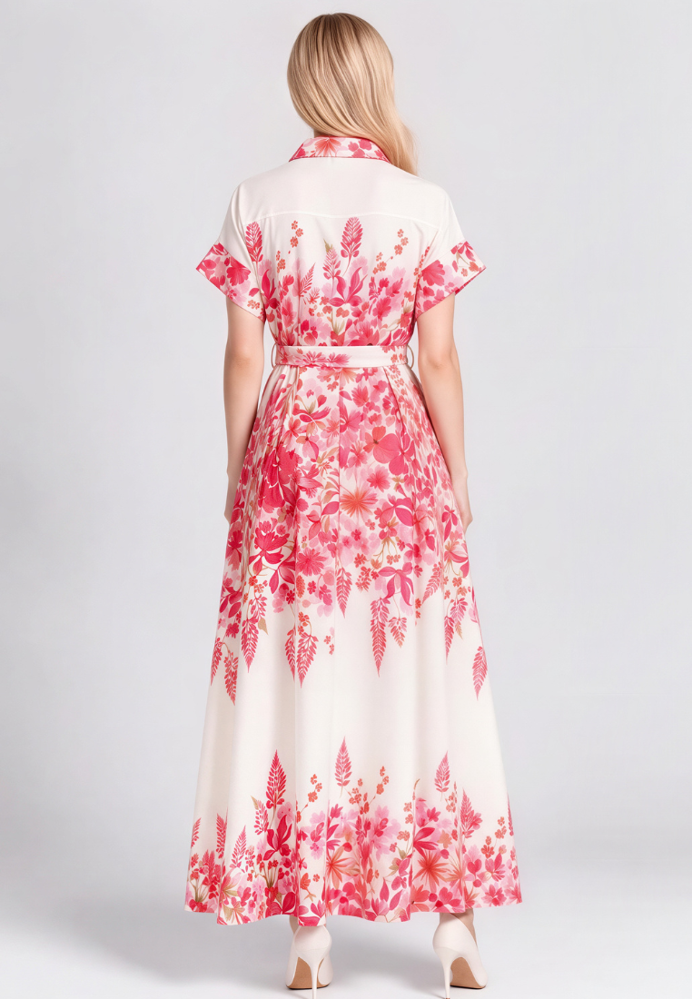A woman viewed from the back wearing a cream-colored maxi dress with a vibrant pink and red floral print, featuring short sleeves and a matching waist tie, set against a plain light gray studio background.