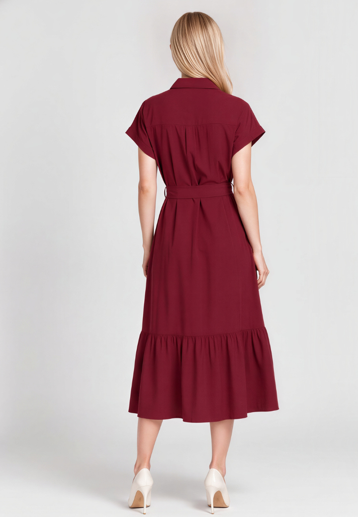A woman viewed from the back wearing a short-sleeve collared midi dress in deep burgundy with a matching waist tie and ruffled hem, paired with white heels, against a light gray studio background.
