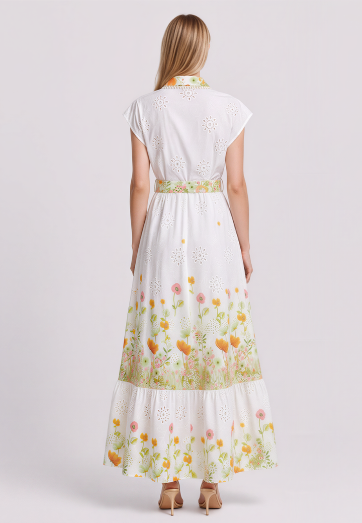 A woman viewed from the back wearing a white eyelet maxi dress with a floral print and a matching waistband, paired with tan high heels, against a light gray studio background.