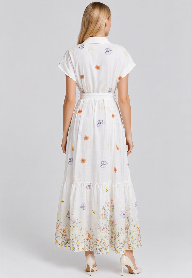 A woman viewed from the back wearing a white short-sleeve maxi dress with a matching waist tie and a multicolor floral print, paired with beige high heels against a light gray studio background.