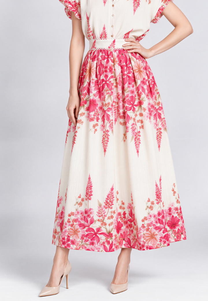 A woman modeling a cream-colored midi skirt with a vibrant pink and red floral print, paired with beige high heels against a light gray studio background.
