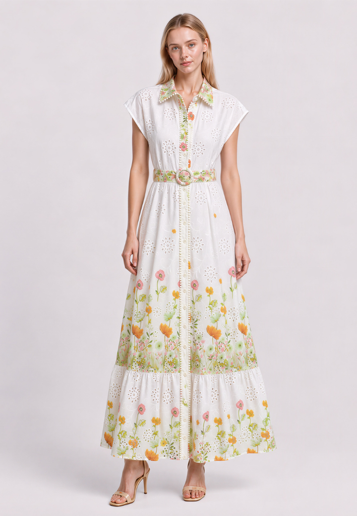 A woman models a white eyelet maxi dress with a green and orange floral print, featuring a button-up front, short cap sleeves, and a matching fabric belt with buckle.